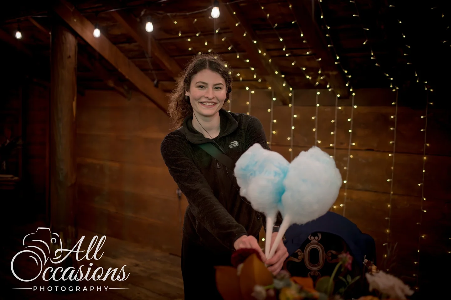 Serena smiling and holding blue cotton candy beneath string lights at a celebration.